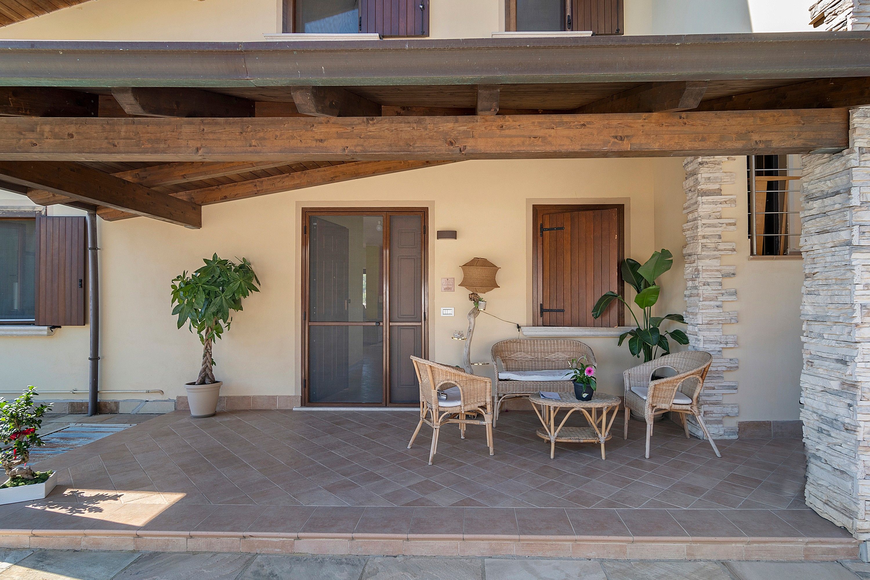 Un patio cubierto con piso de piedra, vigas de madera y mobiliario de mimbre.