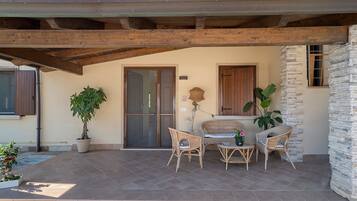 Un patio cubierto con piso de piedra, vigas de madera y mobiliario de mimbre.