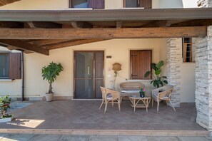A covered patio with a stone floor, wooden beams, and wicker furniture. - Apartment 'La Radice' with Mountain View, Wi-Fi and Air Conditioning (Agropoli)