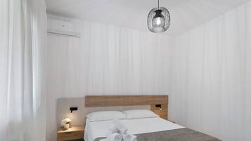 Et moderne hotelværelse med sengegavl i træ, en pænt redt seng med hvide sengetøj, et lille natbord med lampe og en hængende lampe.