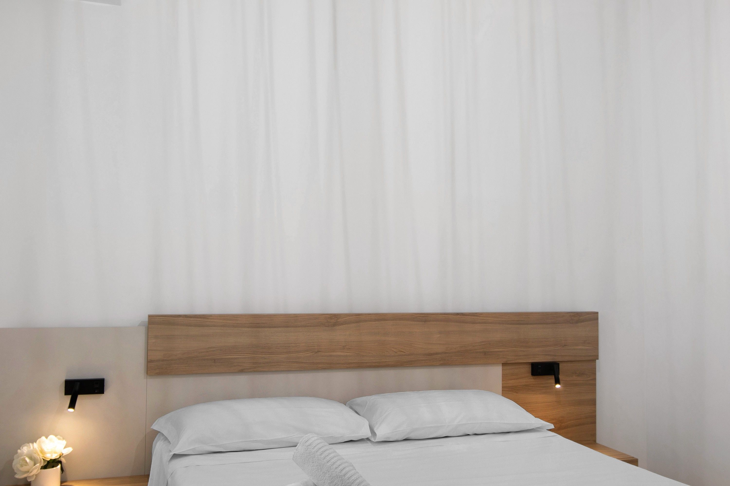 Un dormitorio moderno con cabecera de madera, ropa de cama blanca y dos lámparas de noche.