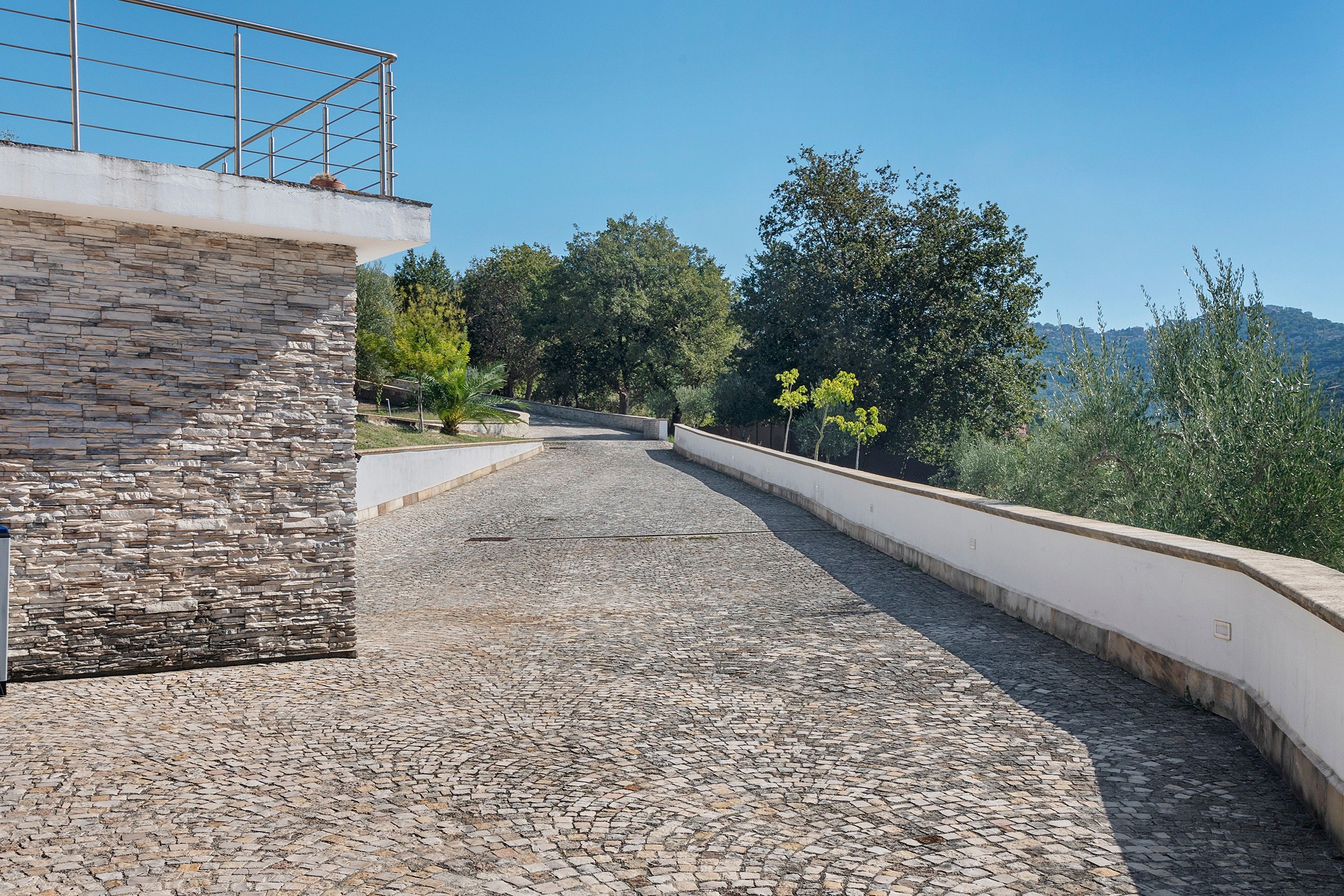 Un sentier pavé de pierres menant à un bâtiment en pierre, agrémenté d’une rambarde métallique au niveau supérieur.