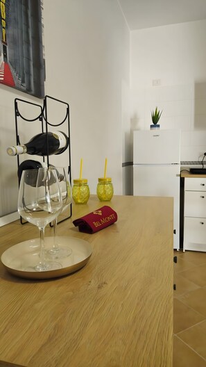Une cuisine avec une table en bois, un verre à vin, deux bocaux en verre avec des couvercles jaunes et une boîte rouge portant l’inscription « BEL MONTE ».
