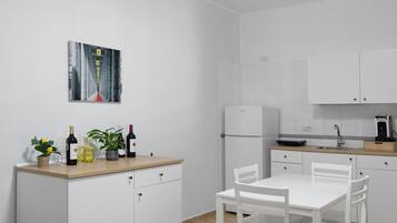 Una cocina moderna con armarios blancos, una mesa de comedor con sillas, una cafetera y una botella de vino sobre la encimera.