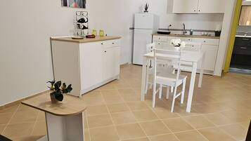Une cuisine moderne avec des meubles blancs, un coin repas avec des chaises blanches et une petite table agrémentée d’une plante.