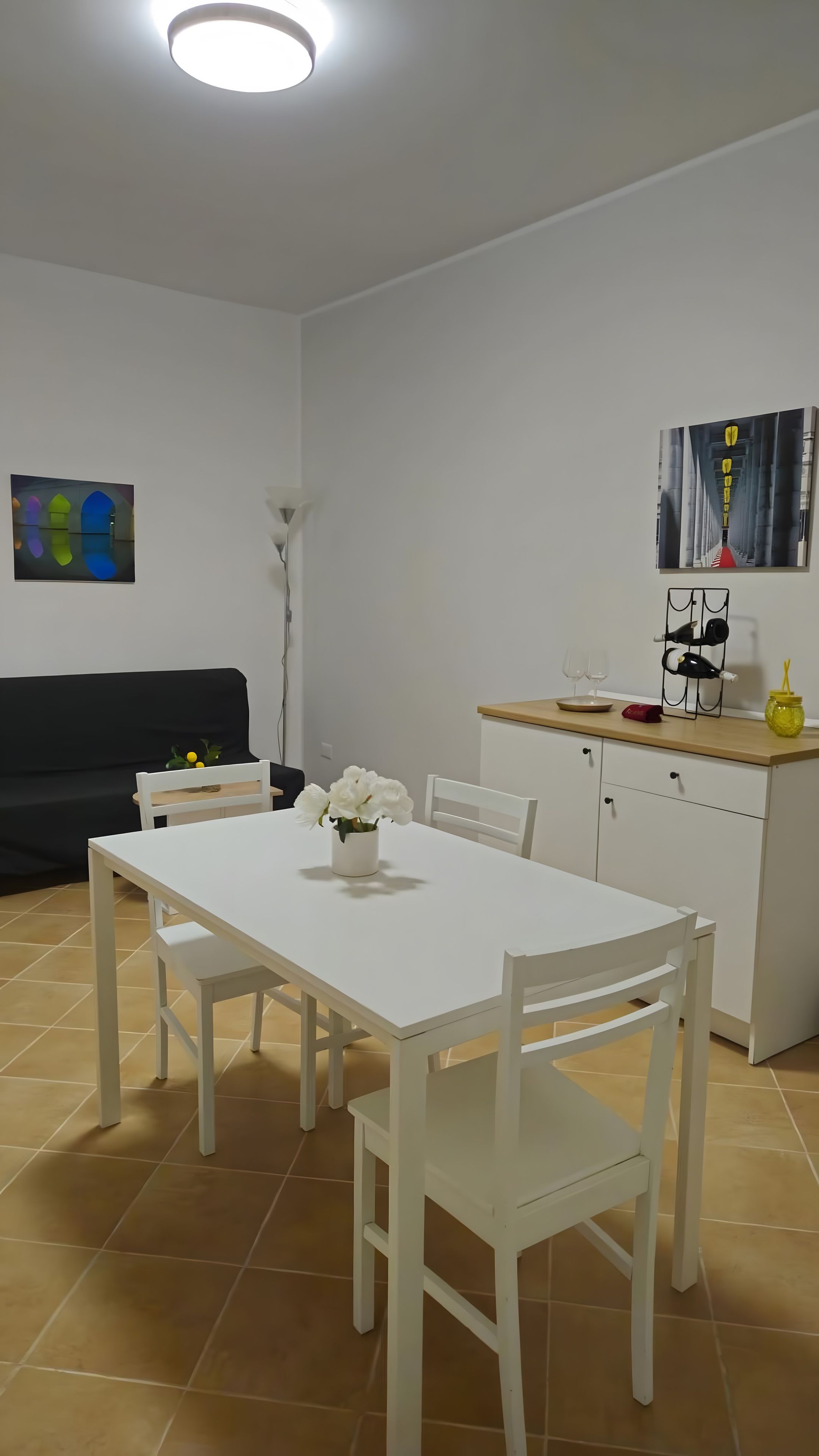 Una cocina moderna con armarios blancos, una mesa de comedor con sillas, un sofá negro y obras de arte en las paredes.