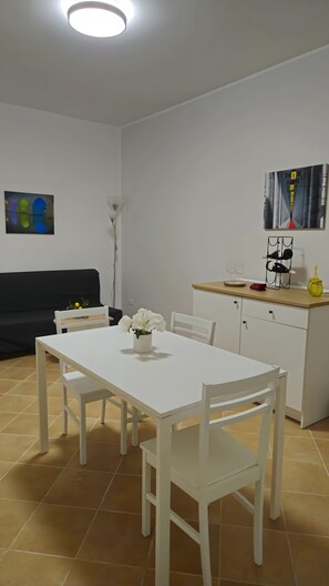 Une cuisine moderne avec des meubles blancs, une table à manger avec des chaises, un canapé noir et des œuvres d’art accrochées aux murs.