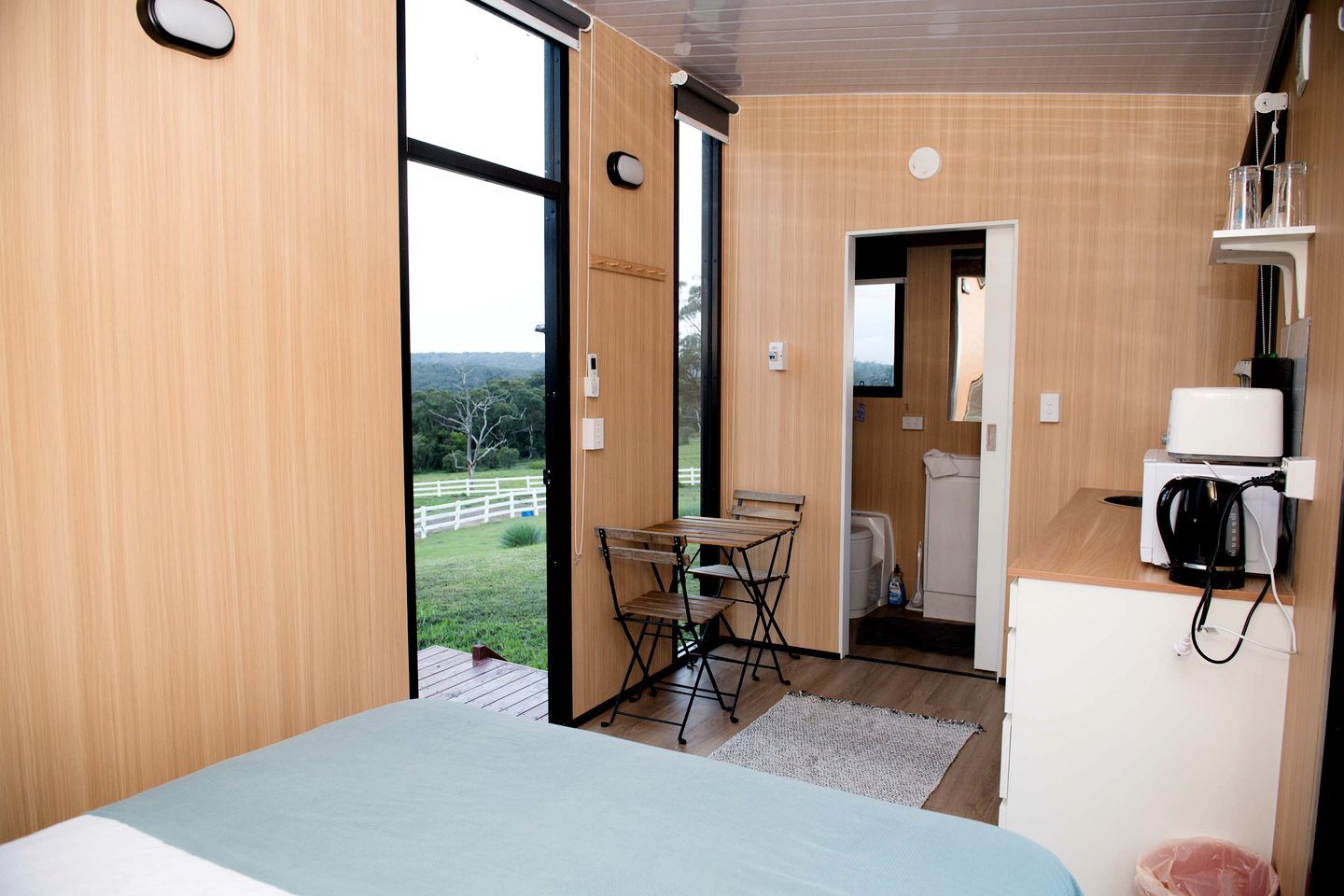 A compact room with a bed, a small table, and a view of the outdoors.