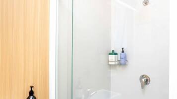 A modern bathroom with a glass shower enclosure, a white sink, and a wooden wall.
