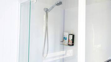 A glass-enclosed shower with a handheld showerhead and a glass shelf with toiletries.