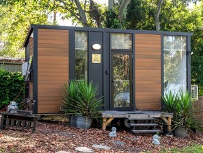 A small wooden cabin with a sliding glass door, a bench, and potted plants.