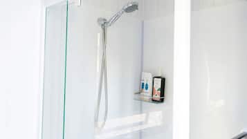 A glass-enclosed shower with a handheld showerhead and a glass shelf with toiletries.