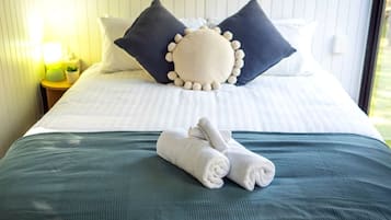 A neatly made bed with pillows and rolled towels, a bedside lamp, and a window with daylight.