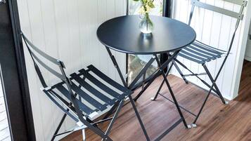 A small round table with a vase of flowers, two black metal chairs, and a wooden floor.