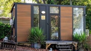 A small wooden cabin with a sliding glass door, a bench, and potted plants.