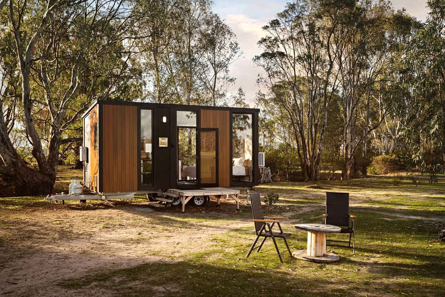 A modern, compact cabin with a sliding door, a small deck, and a dining area with outdoor furniture.