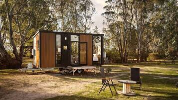 A modern, compact cabin with a sliding door, a small deck, and a dining area with outdoor furniture.
