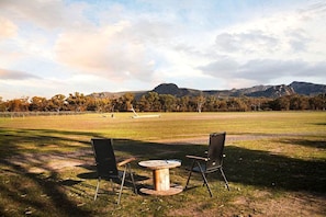 An outdoor seating area with two chairs and a small round table, set against a backdrop of a grassy field and distant mountains.