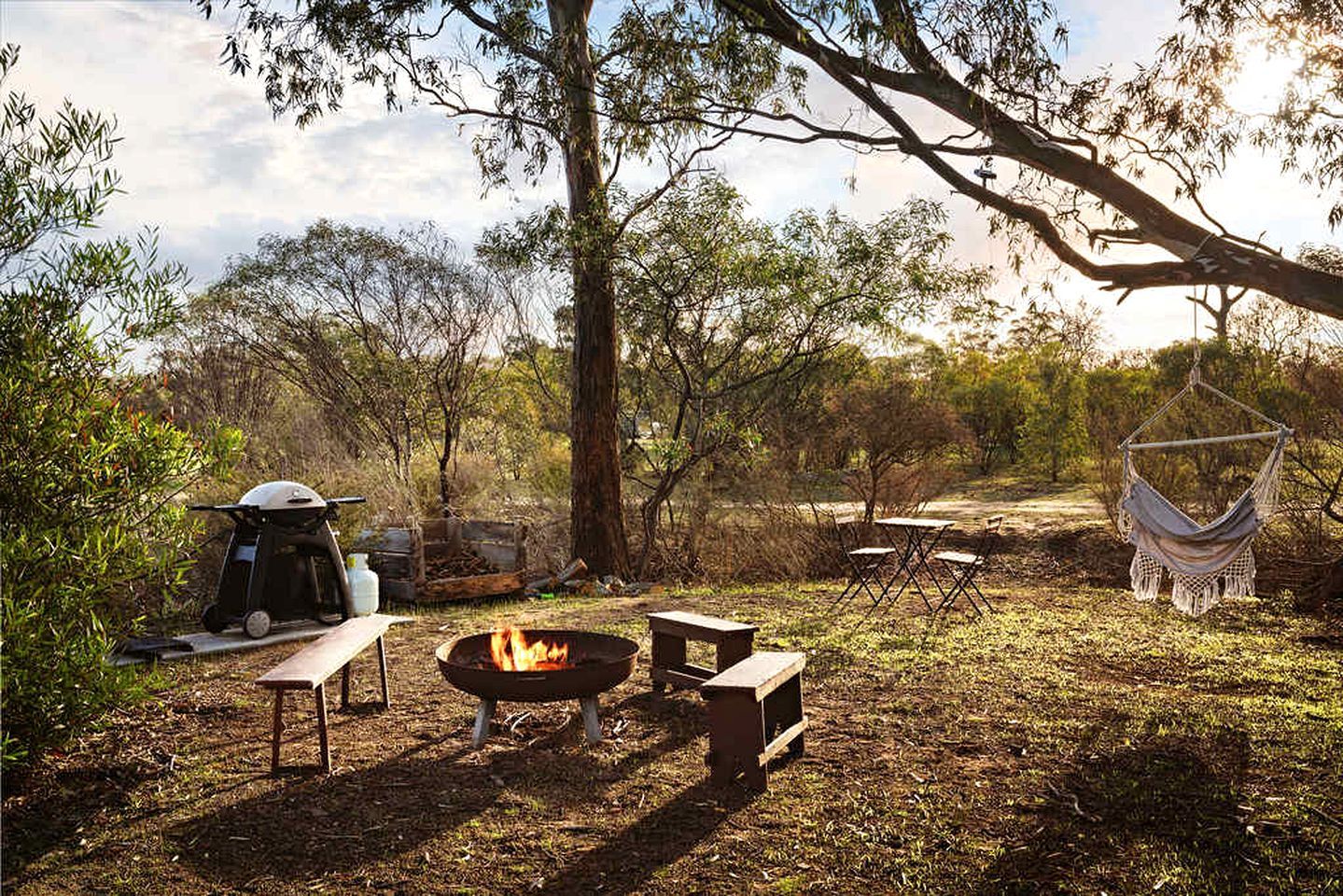 Un camping con un brasero, mesas de picnic, una hamaca y una tienda de campaña.
