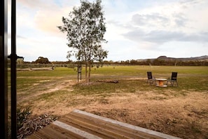 An outdoor area with a wooden deck, two chairs, a table, and a tree.