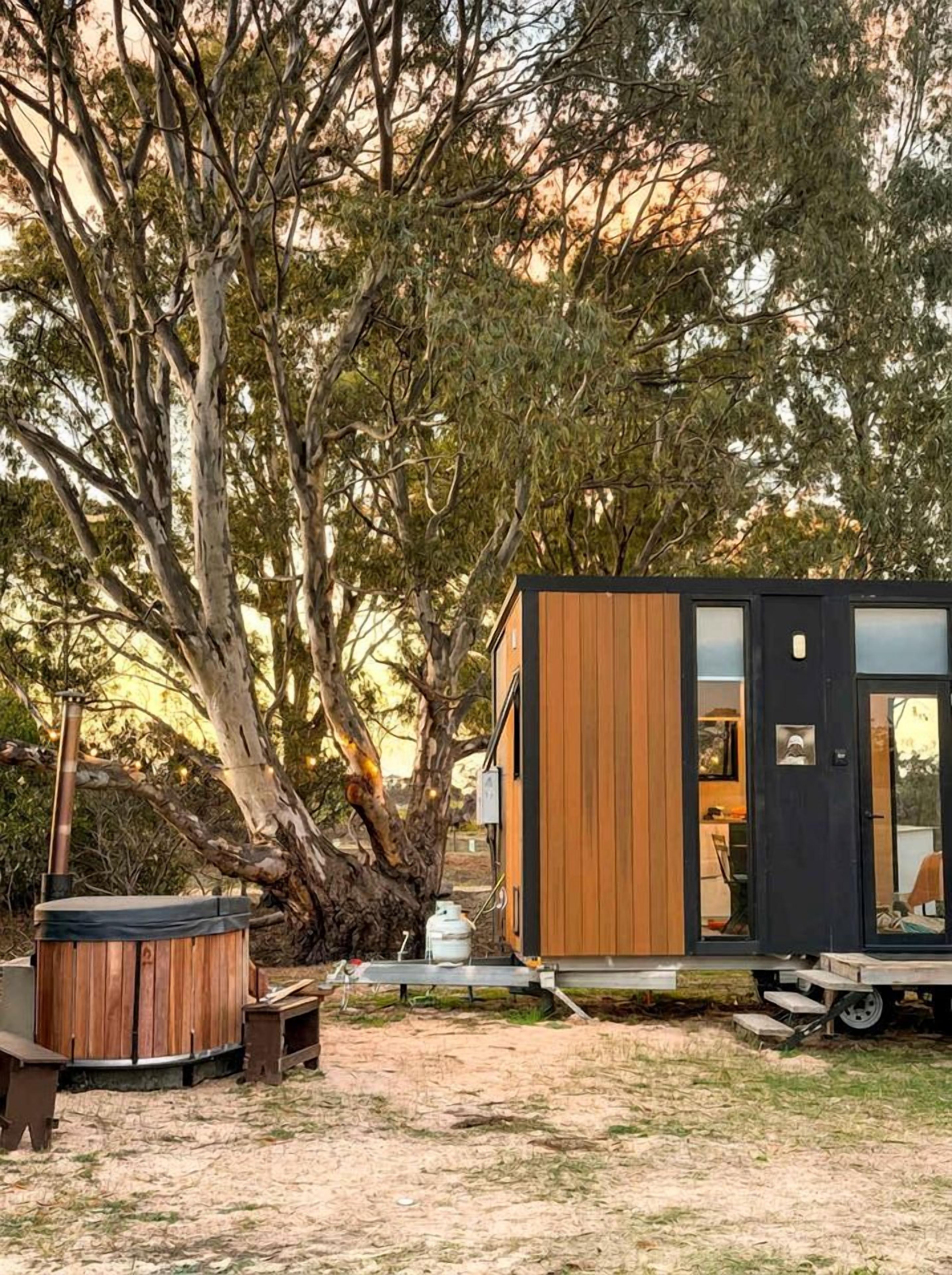Una petita cabana de fusta amb una porta de vidre, en un entorn natural ple d'arbres i una banyera d'hidromassatge.