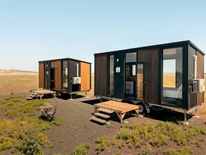 Two modern, compact cabins with external air conditioning units, wooden decks, and a clear view of the surrounding landscape.