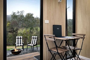A room with a view of a grassy landscape, a table with chairs, a fire pit, and a black box on the wall.
