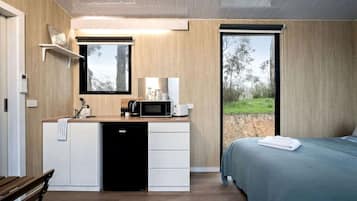 A modern bedroom with a bed, a built-in desk with a microwave, and a view of the outdoors.