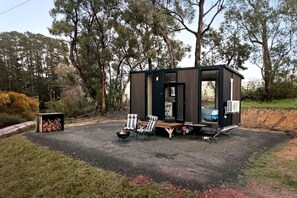 Una cabaña pequeña y moderna con una fogata, zona de estar y una puerta a la vista.
