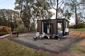 A small, modern cabin with a fire pit, seating area, and a visible door.