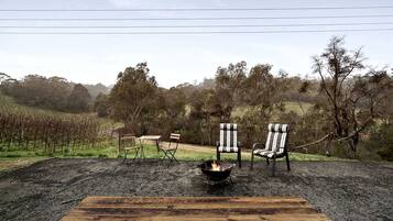 An outdoor seating area with a fire pit and chairs, surrounded by a vineyard and trees.