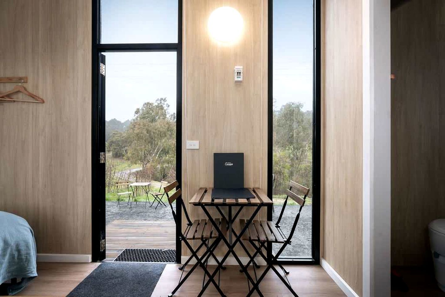 A modern room with a wooden floor, a desk with a laptop, a chair, and a bed.