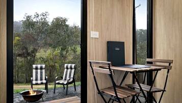 Une pièce avec vue sur un paysage verdoyant, une table avec des chaises, un foyer et une boîte noire fixée au mur.