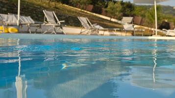 En klar swimmingpool med liggestole og parasoller.