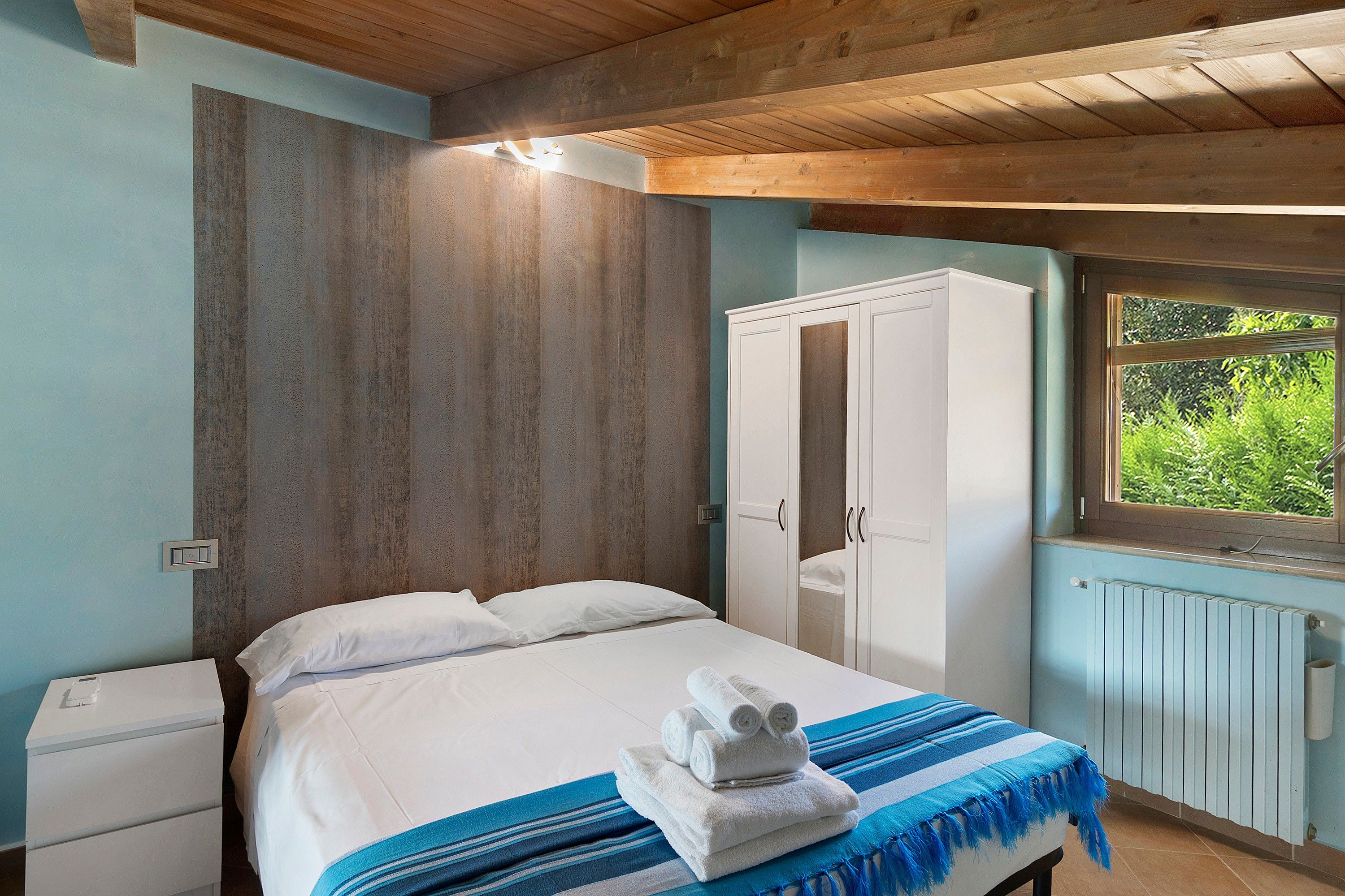 Une chambre à coucher avec un lit, une armoire, une fenêtre donnant sur un beau paysage et un radiateur.