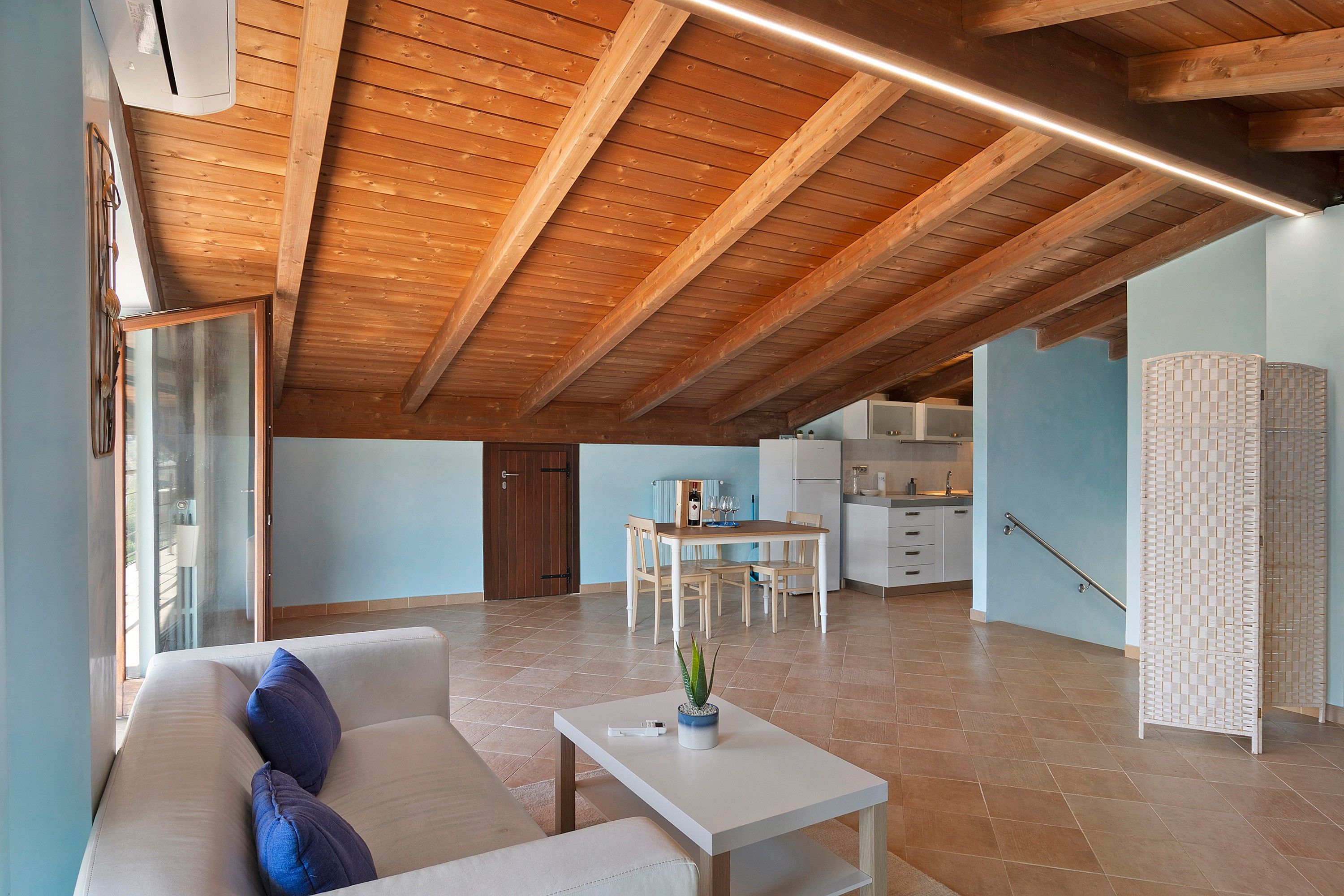 A spacious living area with a high wooden ceiling, a dining table, and a sofa with cushions.