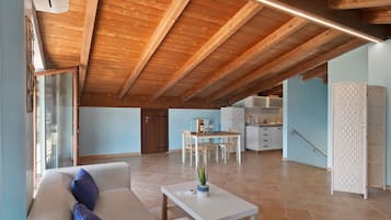 A spacious living area with a high wooden ceiling, a dining table, and a sofa with cushions.