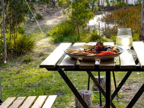 A picnic table with a plate of food and a glass of white beverage, set against a natural backdrop.