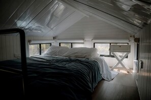 A single bed in a room with a sloped ceiling, a window, and a small table.