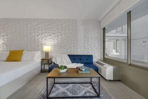 A modern room with a patterned wall, a blue sofa, a white bed, a wooden coffee table, and a window with a view. - Disney Getaway w/ Resort Vibes + Parking | Orl (Kissimmee)