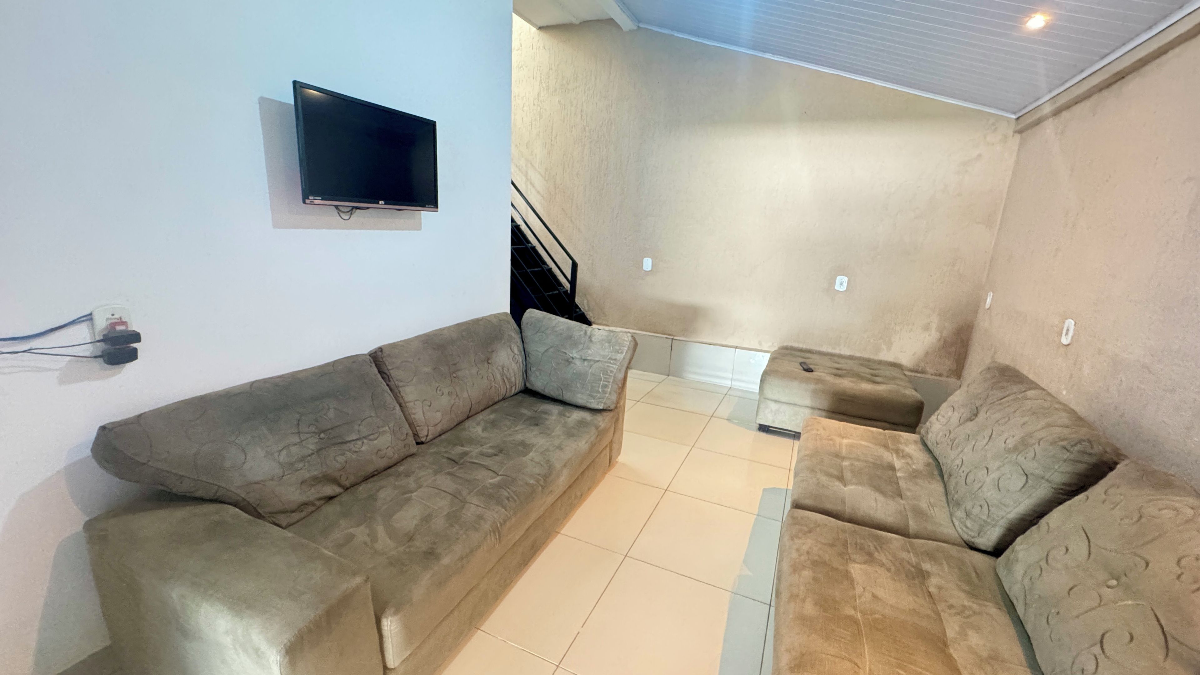 A living room with a sofa, ottoman, and a flat-screen TV mounted on the wall.