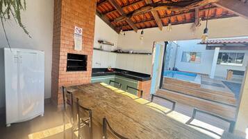Una cocina con horno de ladrillo, refrigerador y comedor con mesa y sillas de madera.