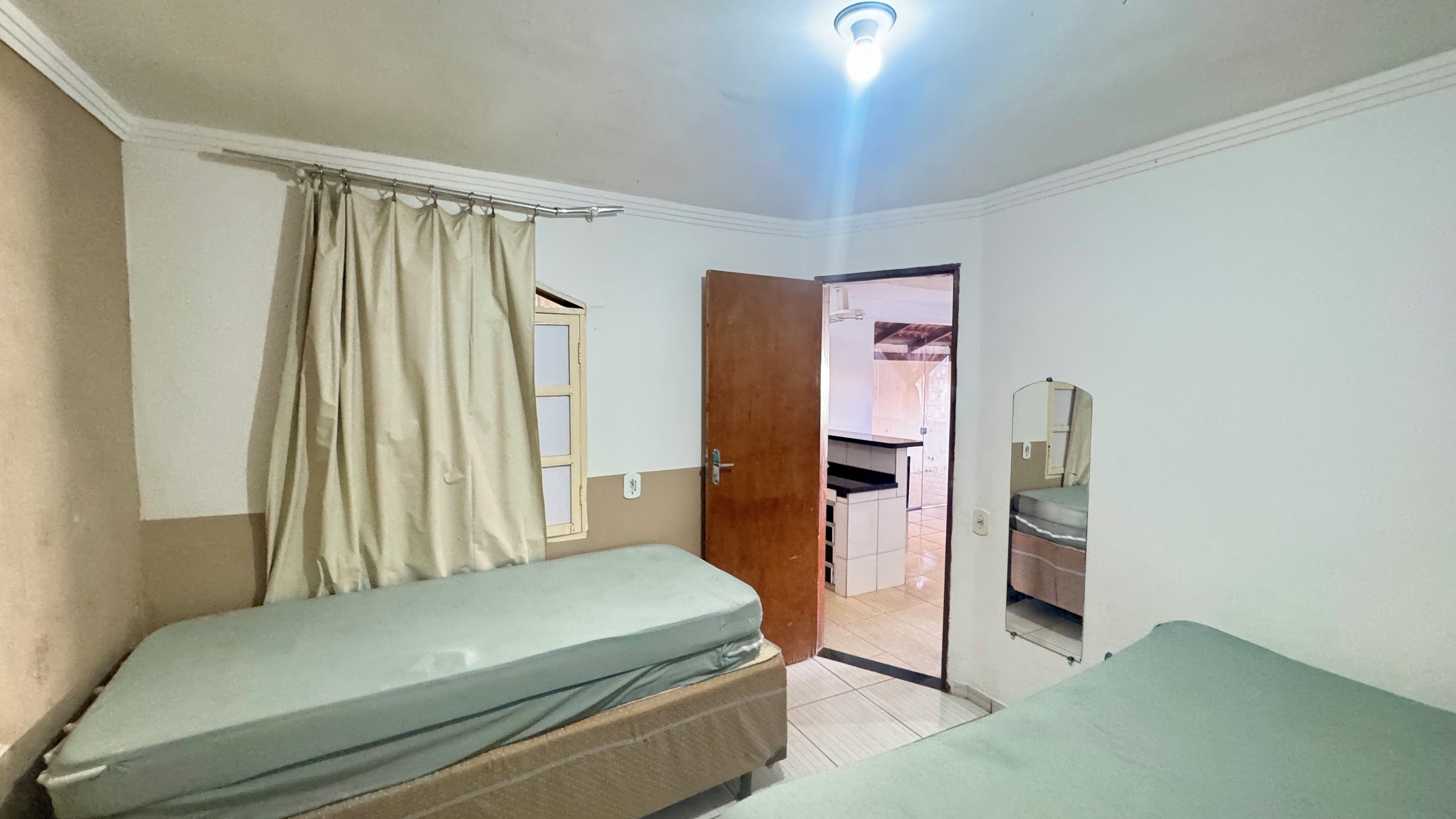 A room with two beds, a wooden door, a mirror, and a light fixture.