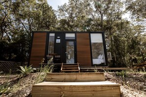 A modern, compact cabin with a wooden exterior, a glass door, and a small outdoor seating area. - Fantastic Tiny House Retreat with Vineyards Views in Anna Bay, New South Wales (Anna Bay)