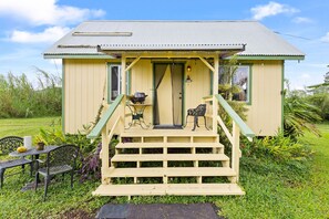A small, single-story house with a porch, a table and chairs, and a garden. - Peaceful Eco-Farm A-Frame in Keaau,Volcano & Beach (Keaau)