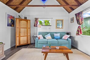 A cozy living room with a teal sofa, wooden cabinet, and a coffee table. - Peaceful Eco-Farm A-Frame in Keaau,Volcano & Beach (Keaau)