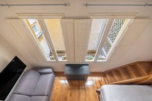 Ein Zimmer mit Holzboden, einem grauen Sofa, einem Flachbildfernseher und einer Treppe.