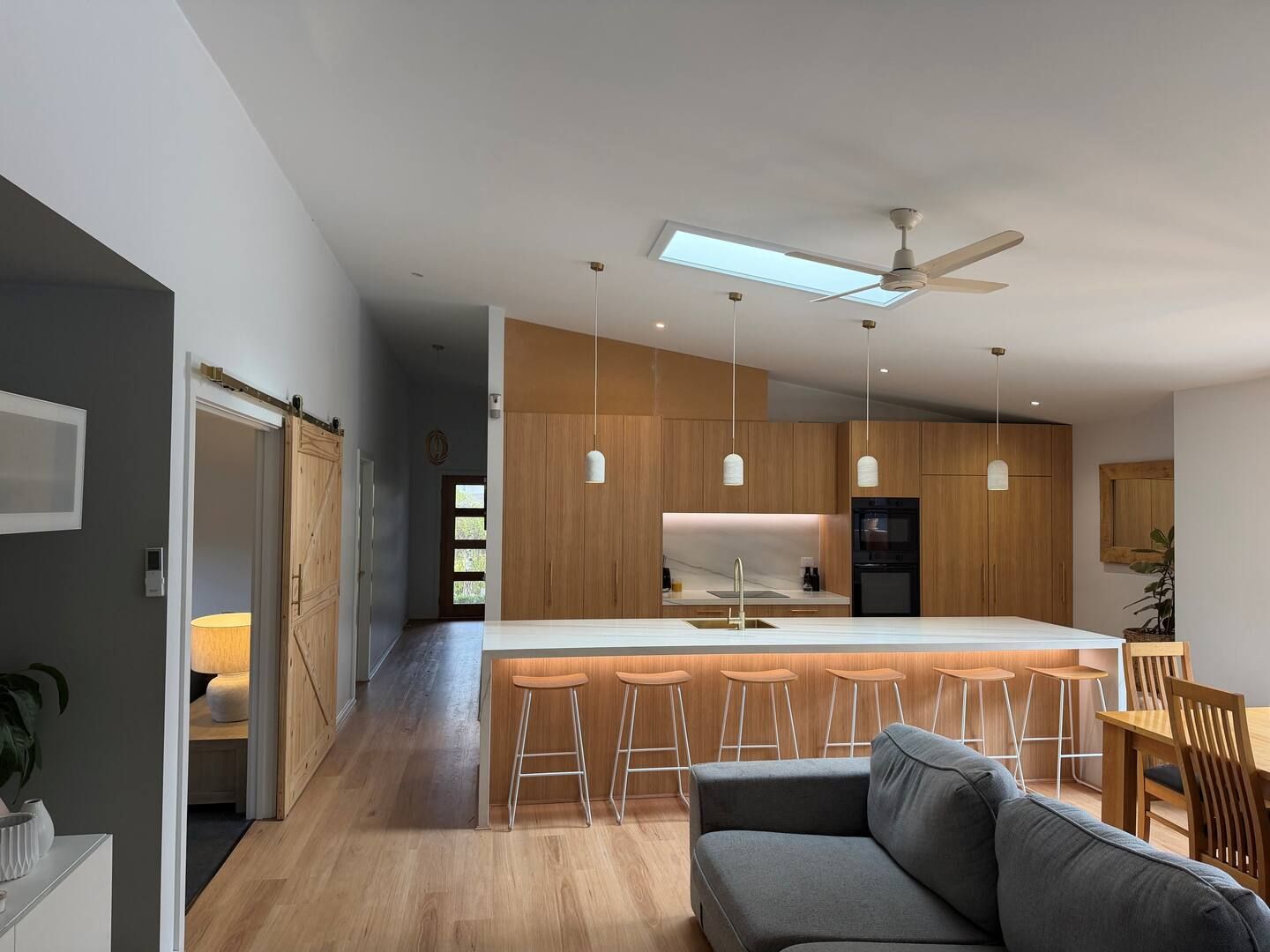 A modern kitchen with a central island, bar stools, and a ceiling fan.