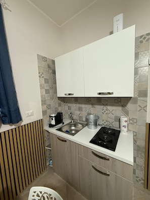 A compact kitchen with white cabinets, a stainless steel sink, a gas stove, and a coffee maker. - Small house with a garden, parking space, gazebo, tables, chairs, and an outdoor kitchen. (Pagani)