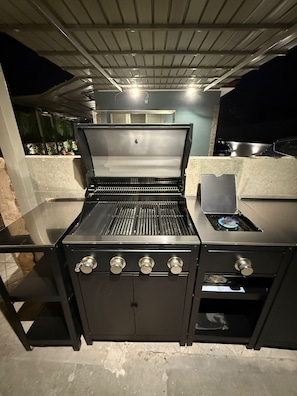 An outdoor kitchen with a grill, a sink, and a gas stove. - Small house with a garden, parking space, gazebo, tables, chairs, and an outdoor kitchen. (Pagani)